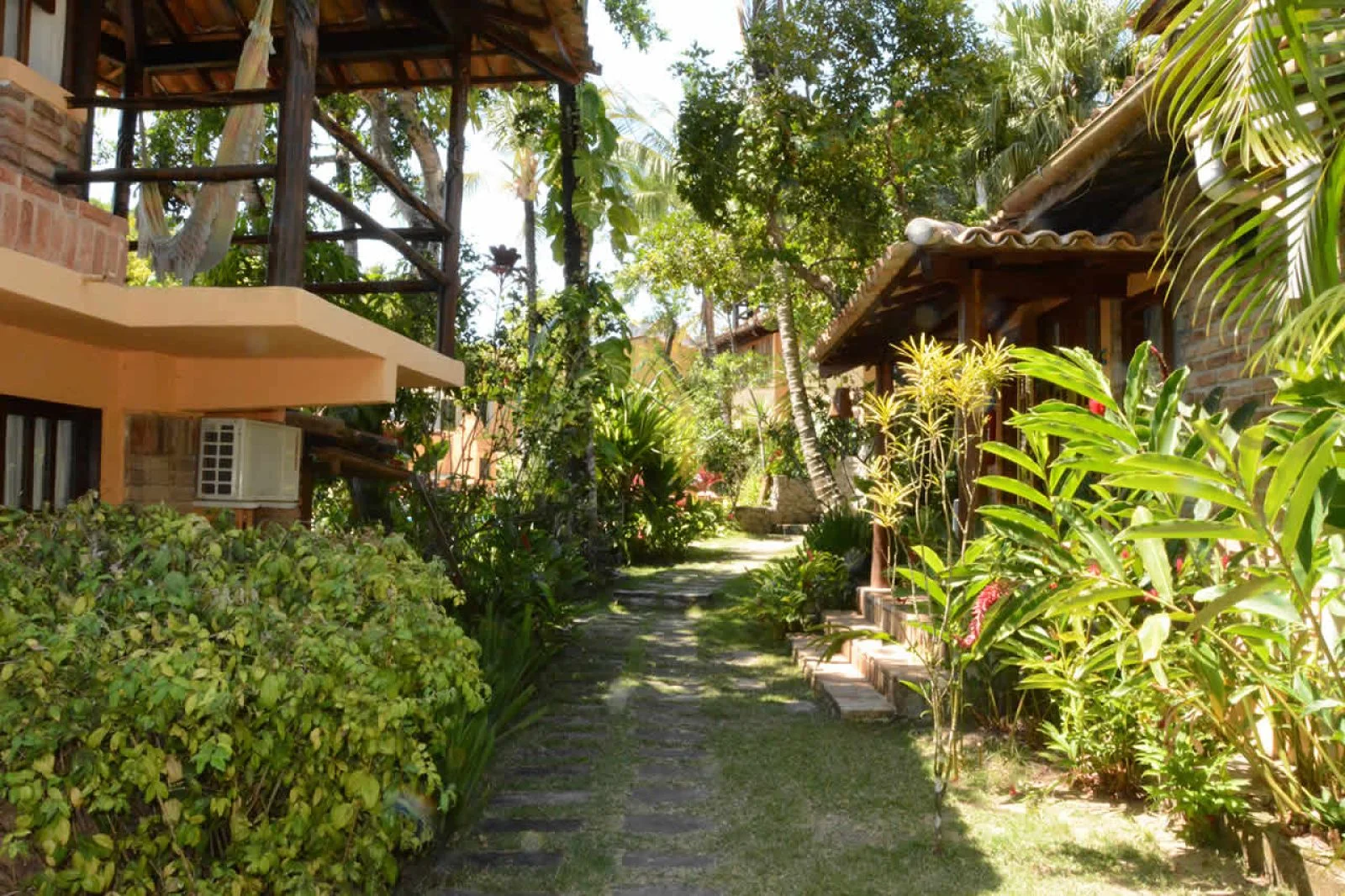 Corredor cercado por flores e plantas tropicais na Pousada 4 Ventos, um refúgio acolhedor entre as pousadas em Arraial d'Ajuda.